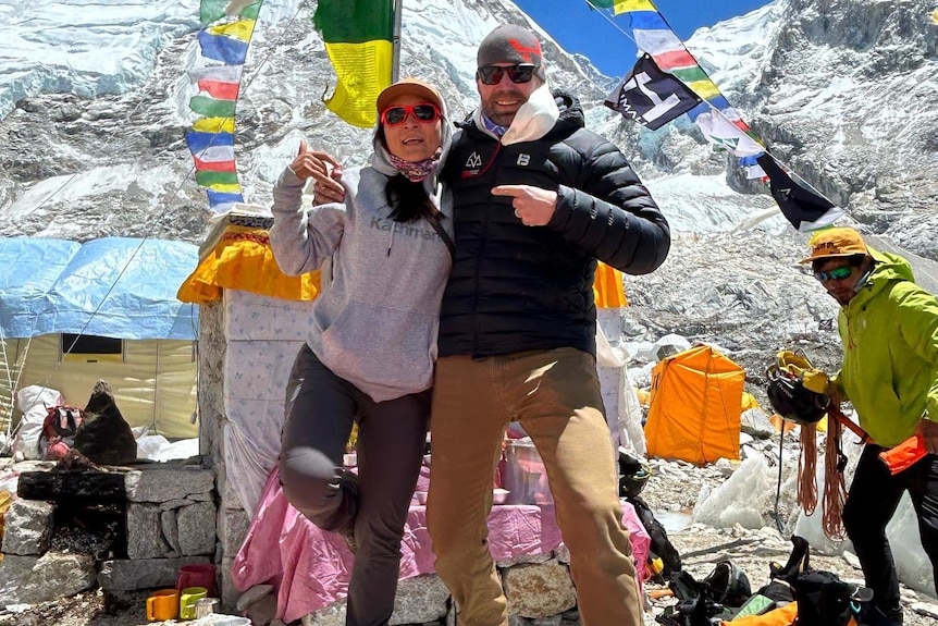 A man and a woman standing at a camp on Mount Everest, with a strong of flags in the background.
