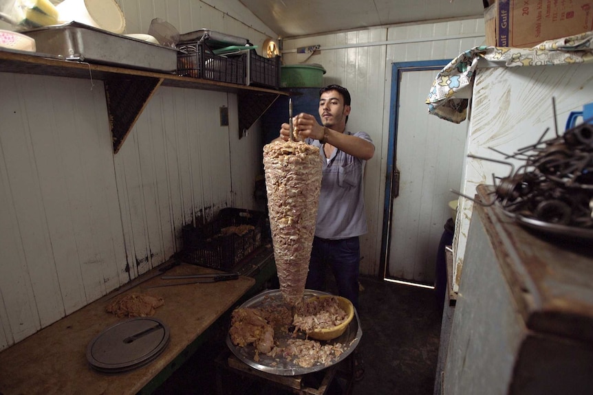 A young Syrian man puts meat on a metal spike.