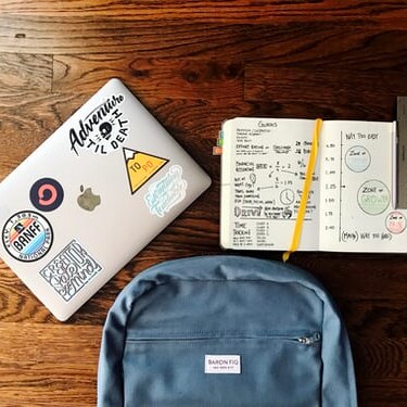 A school bag, pencil case and laptop computer sit on a wooden school desk