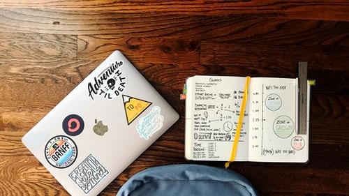 A school bag, pencil case and laptop computer sit on a wooden school desk