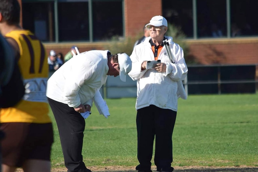 A photo of an older man wearing a white jacket on a football field.