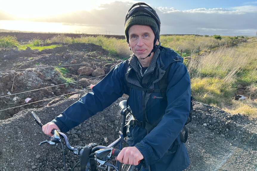 Andrew Booth stands with his bike in front of a field