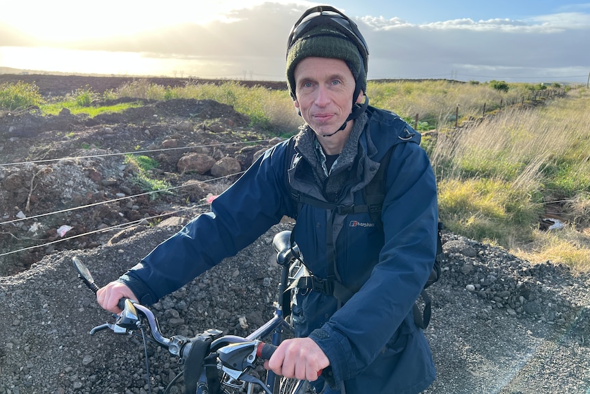 Andrew Booth stands with his bike in front of a field