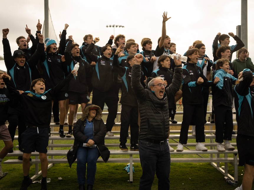 Several dozen fans at a regional football ground stand and cheer