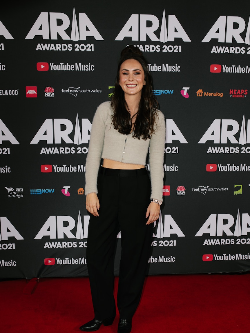 A black haired woman on the red carpet in a beige top.