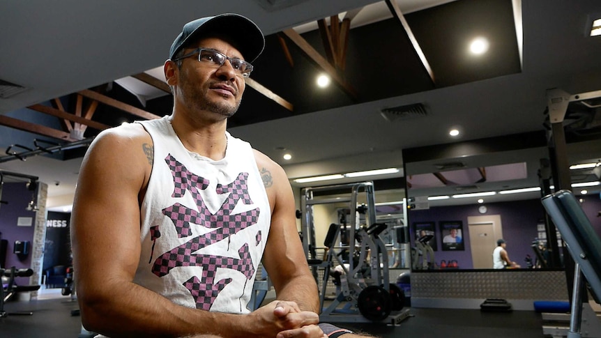 Indigenous man Dale Cameron sits on a gym bench surrounded by gym equipment