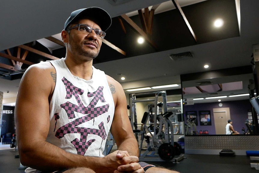 Indigenous man Dale Cameron sits on a gym bench surrounded by gym equipment