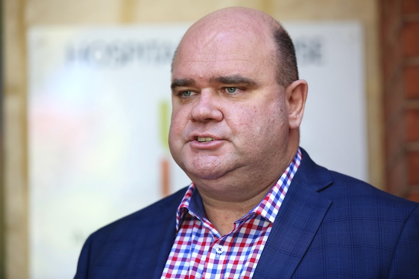 A tight head and shoulders shot of a man in a suit speaking to reporters