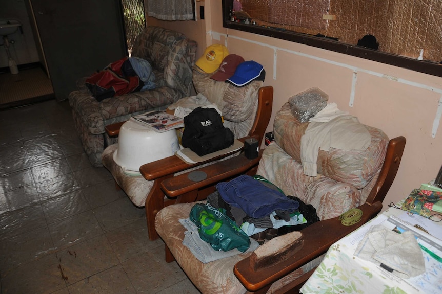 Folded clothes and other stuff sitting on chairs, along with three caps.