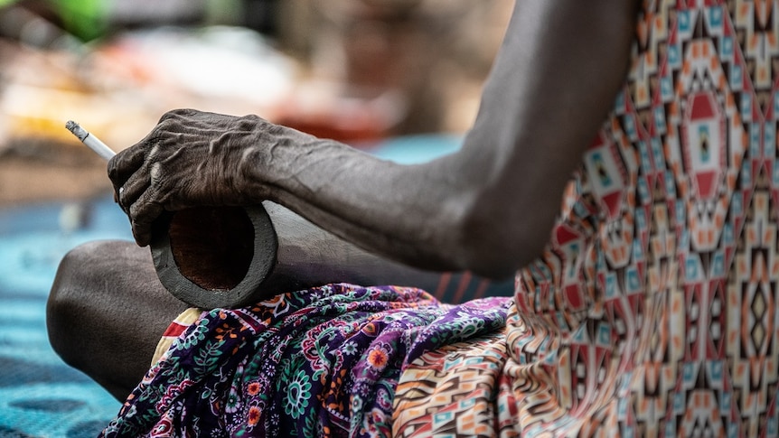 A woman is painting a didgeridoo and smoking a cigarette