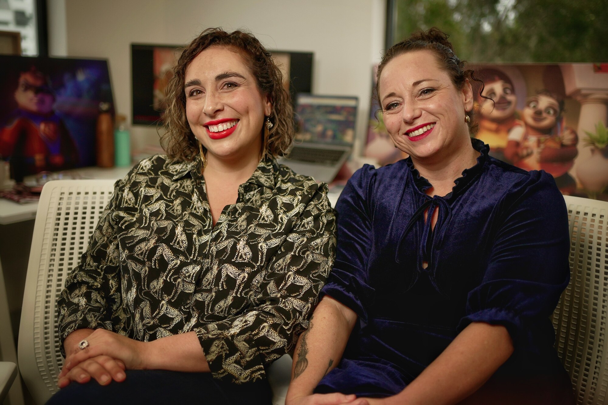 Two women smile at the camera as they sit side-by-side.