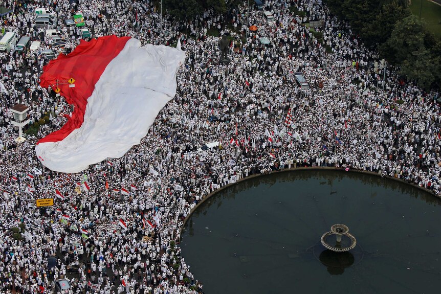 A massive crowd with Indonesian flag standing near a fountain