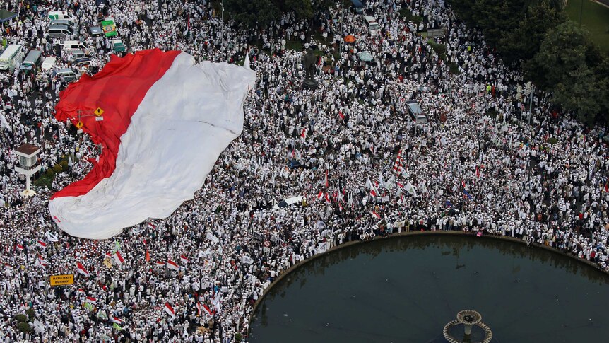 A massive crowd with Indonesian flag standing near a fountain