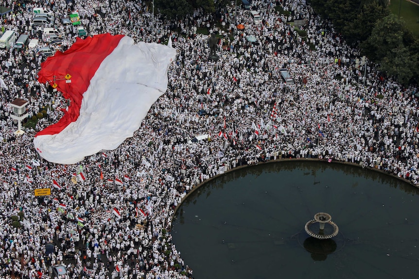 A massive crowd with Indonesian flag standing near a fountain