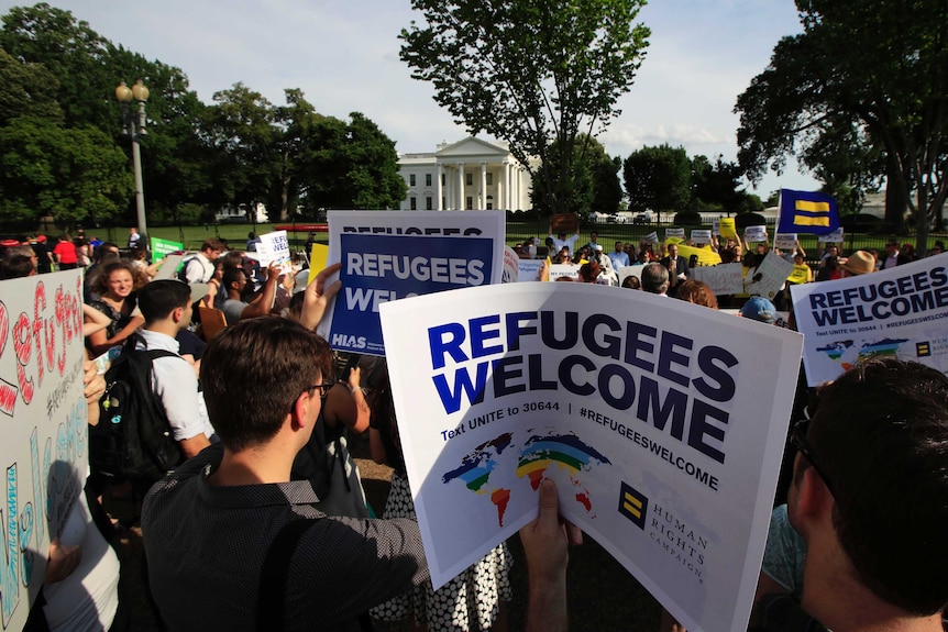 Refugees and community activists gather in front of the White House in Washington holding signs that read "welcome refugees".