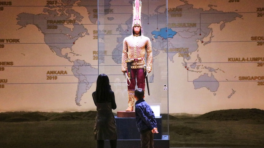 The revered Kazak Golden Man warrior is displayed standing in front of a world map in the national museum