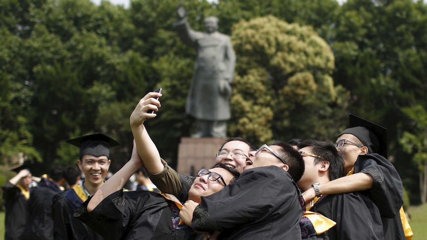 Graduates, in academic dress, take a 'selfie' in front of a statue of late Chinese leader Mao Zedong