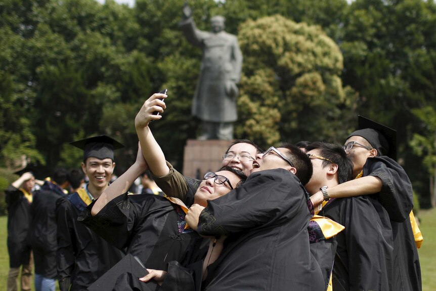 Graduates, in academic dress, take a 'selfie' in front of a statue of late Chinese leader Mao Zedong
