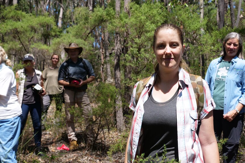 Several women and a man stand in bushland smiling 
