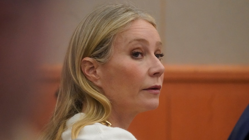 A blonde woman is pictured in a courtroom looking over her right shoulder. 