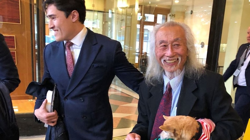 Two smiling men in suits, one holding a small dog.