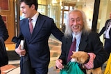 Two smiling men in suits, one holding a small dog.