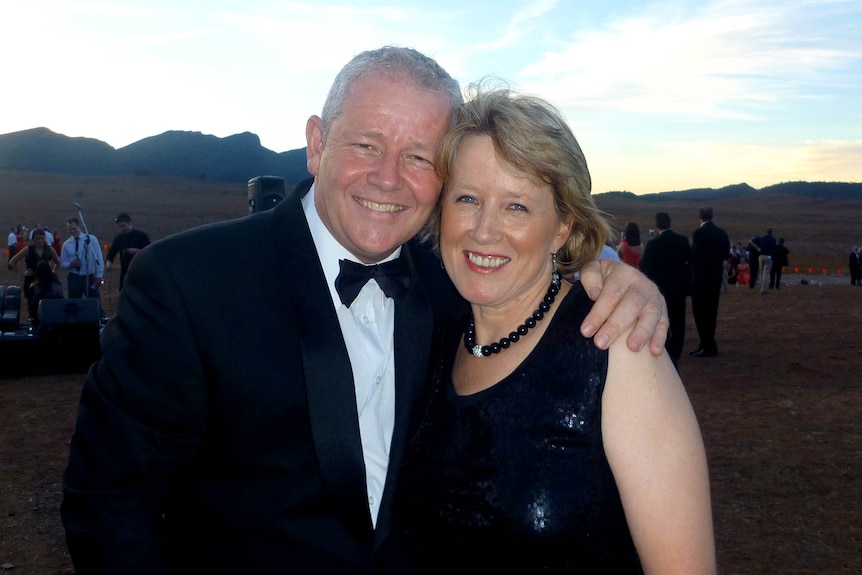 A man and women in black tie dress stand close together in the outback
