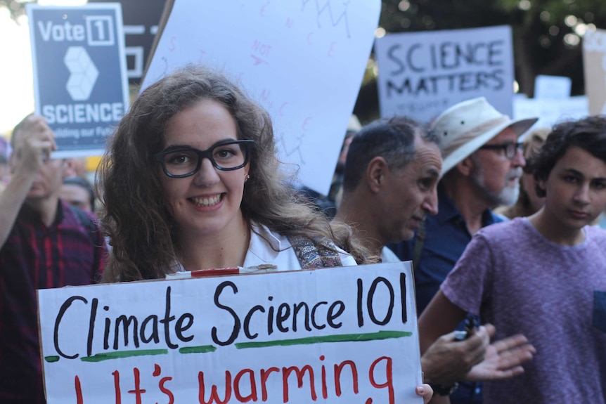 Imogen Wadlow stands among protesters holding a sign reading "Climate Science 101"