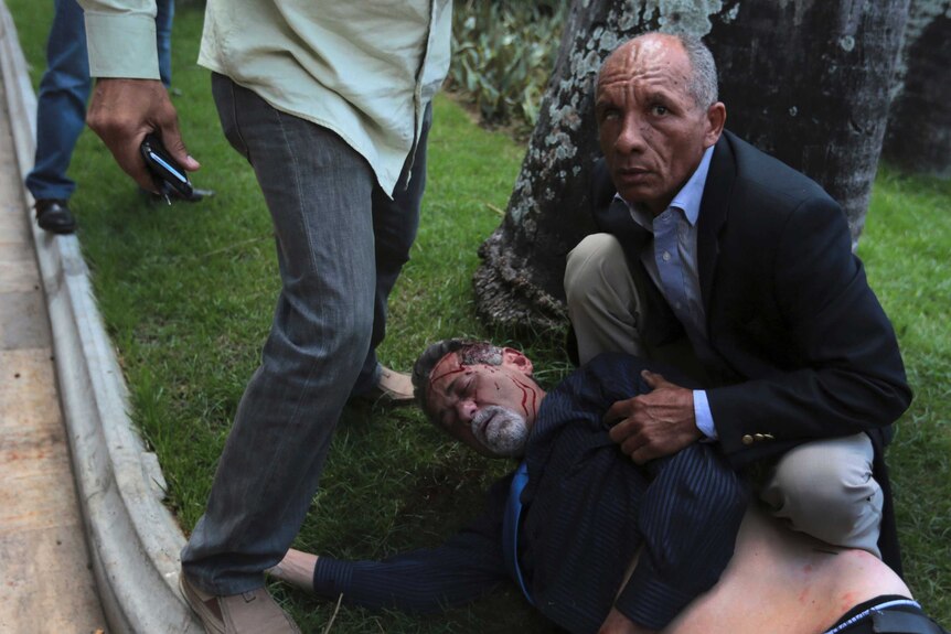 An injured opposition politician lies on the ground with blood dripping from him.