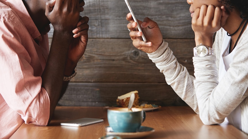 Man and woman sit at cafe table facing one another