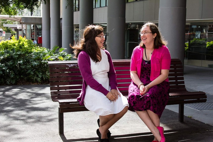 Two women sitting on a public bench outside an office.
