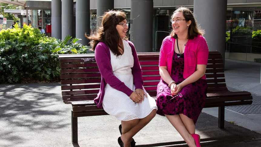 Two women sitting on a public bench outside an office.
