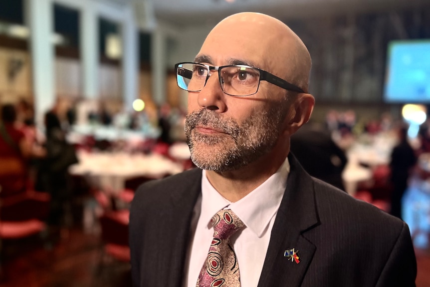 Ian sits at a table at the breakfast wearing a Indigenous pattered tie