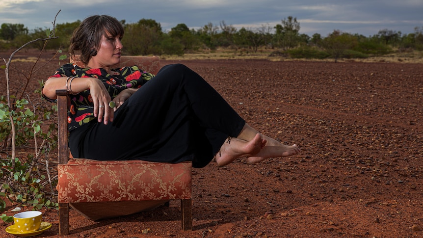 Artistic posed promotional shot of a woman sitting on an armchair in the desert.