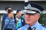 Police Commissioner Chris Dawson in full uniform speaks into microphones at the front of the police headquarters building.