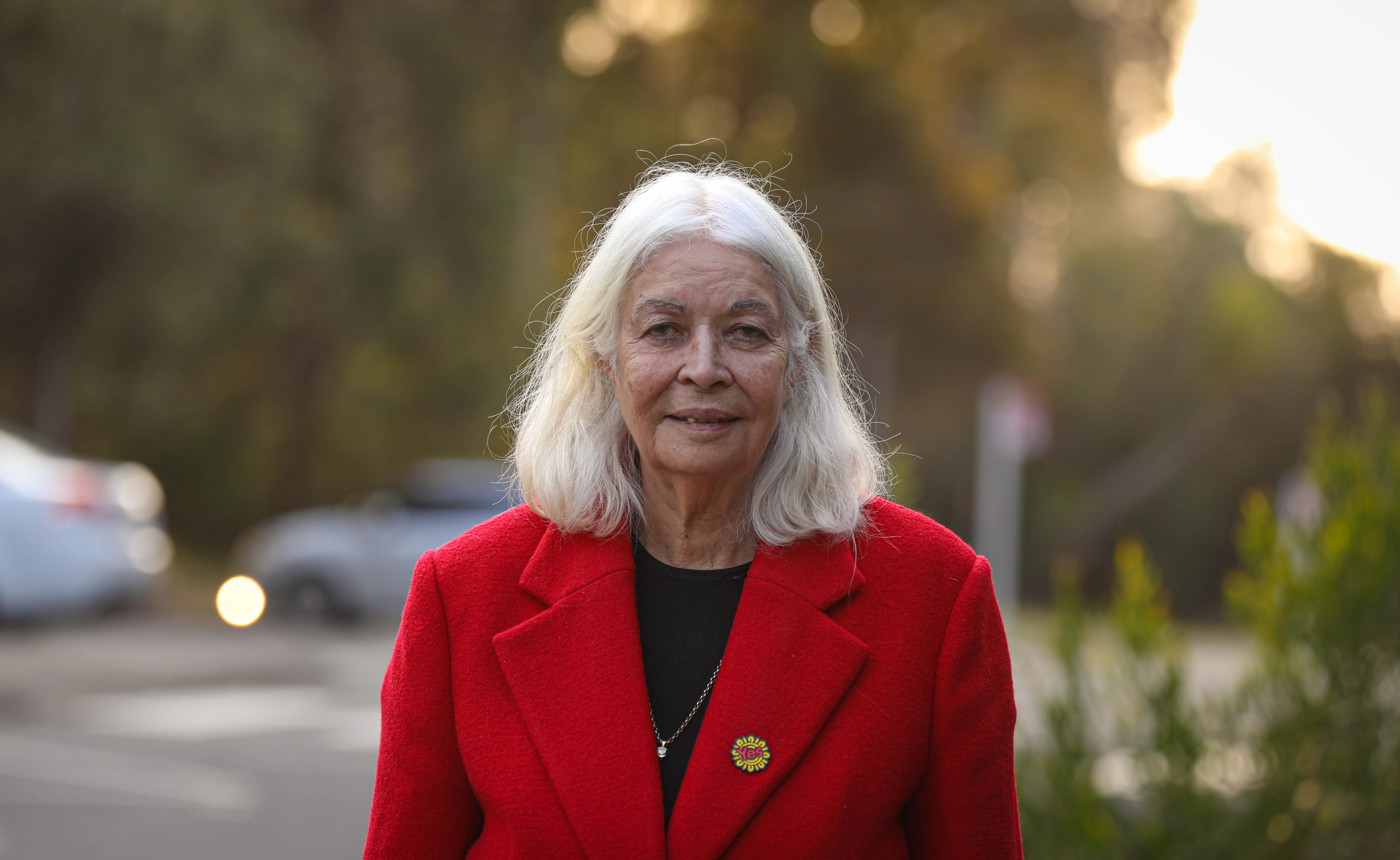 Marcia Langton wears a bright red coat and gives a small smile to the camera.