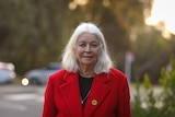 Marcia Langton wears a bright red coat and gives a small smile to the camera.