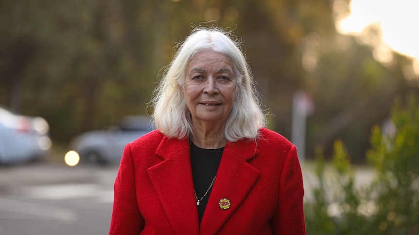 Marcia Langton wears a bright red coat and gives a small smile to the camera.