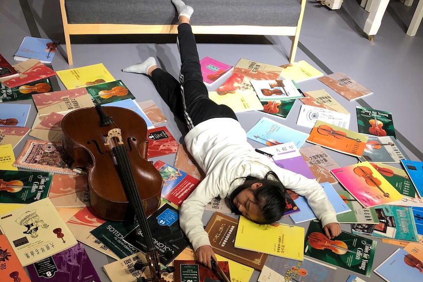 A young cello student posed for the falling stars challenge with her instrument and books on the floor.