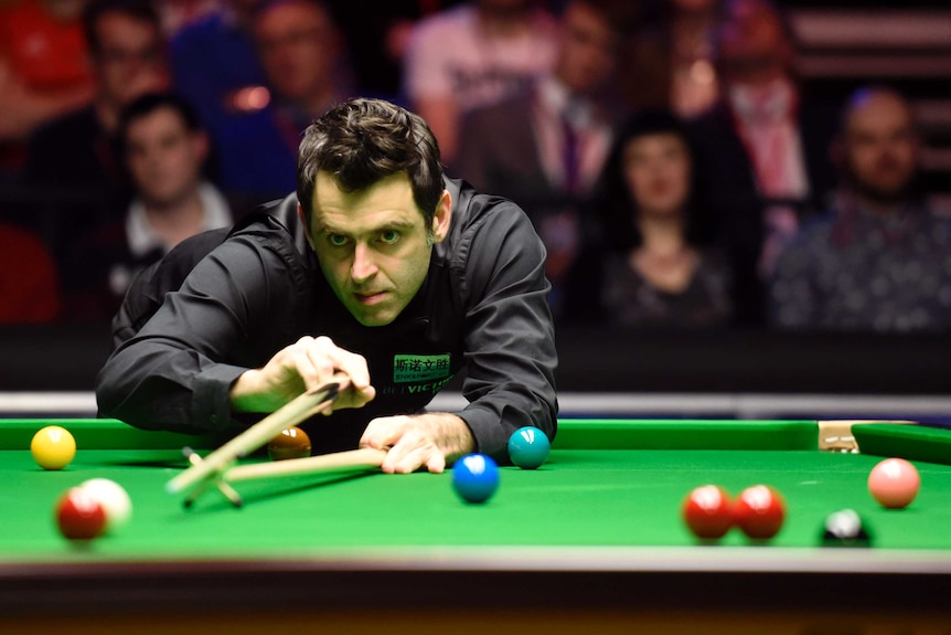 Ronnie O'Sullivan uses the rest to play a shot, leaning over a green snooker table