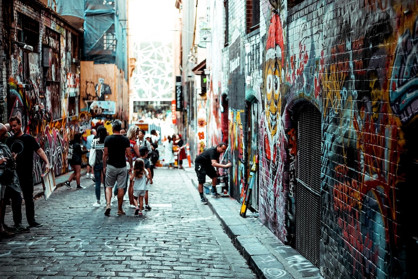 Melbourne lane filled with street art, people and a street artist, some of the benefits of Melbourne over Vienna.