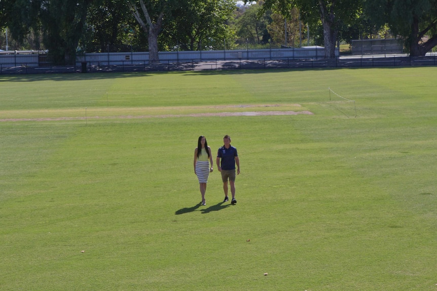 Two people walk across a football oval