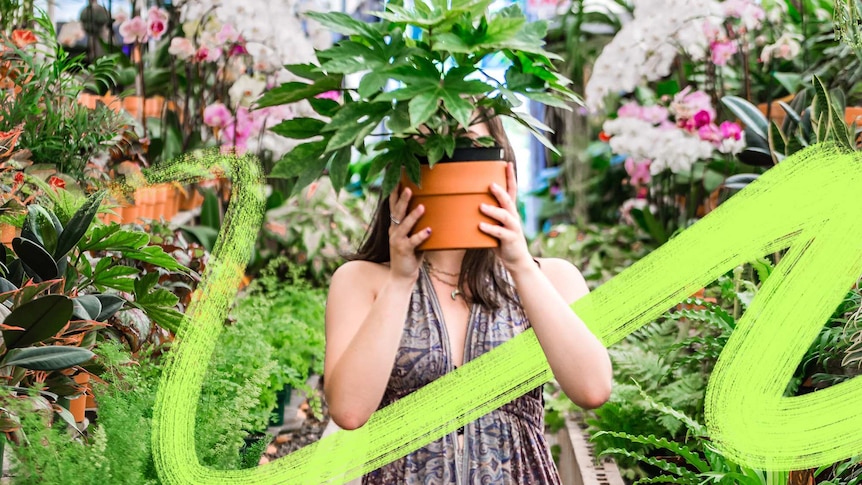 A woman stands in a garden store holding a pot plant in front of her face to depict making gardening mistakes