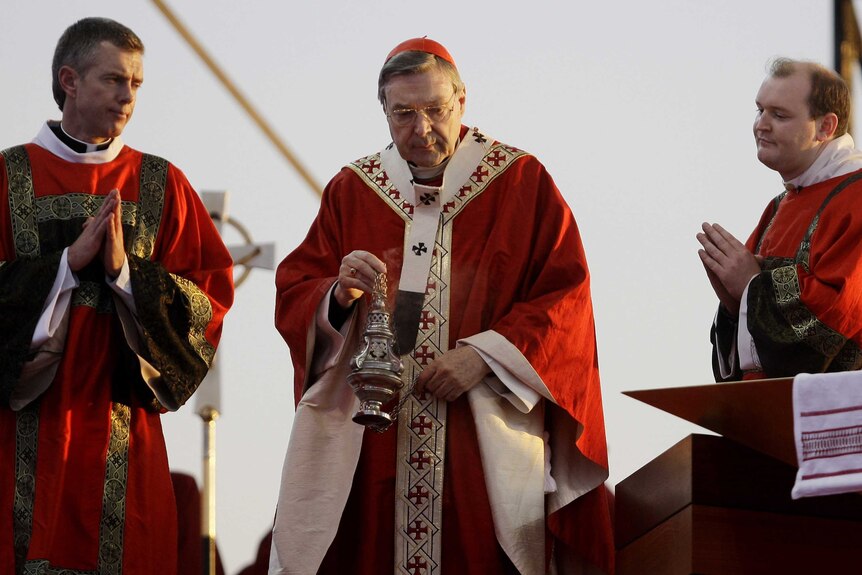 Cardinal George Pell holds incense while standing between two priests at World Youth Day in Sydney