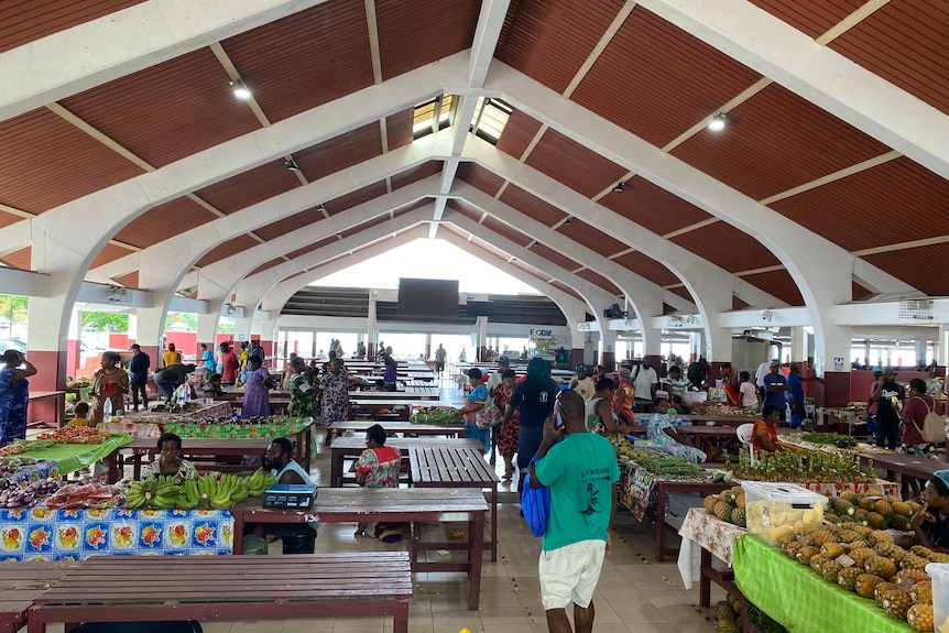 A food market full of people in bright coloured clothes, and vendors selling pineapples, bananas and other crops, in Vanuatu.