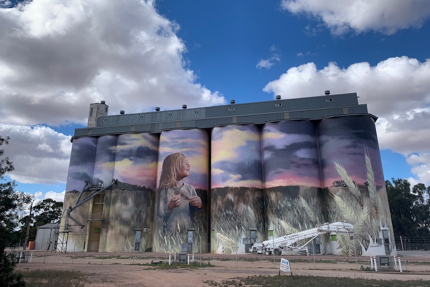 beautiful big grain silos with a purple mural painted on it with a blue sky backdrop. 