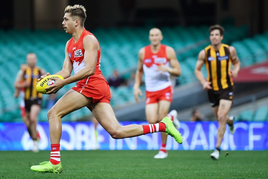A Sydney Swans AFL players runs with the ball in two hands against Hawthorn.