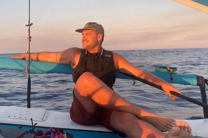 Man sitting on a Hobie Cat at sea, smiling