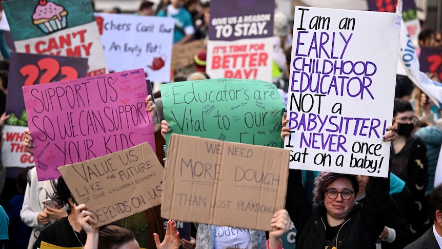 A sea of signs at a childcare protest in Sydney, with one woman's face showing.