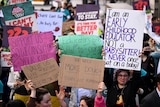 A sea of signs at a childcare protest in Sydney, with one woman's face showing.